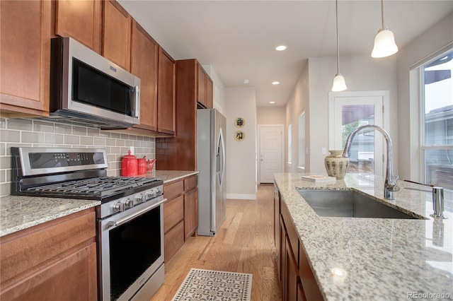 kitchen with stainless steel appliances, light wood-type flooring, pendant lighting, light stone countertops, and sink