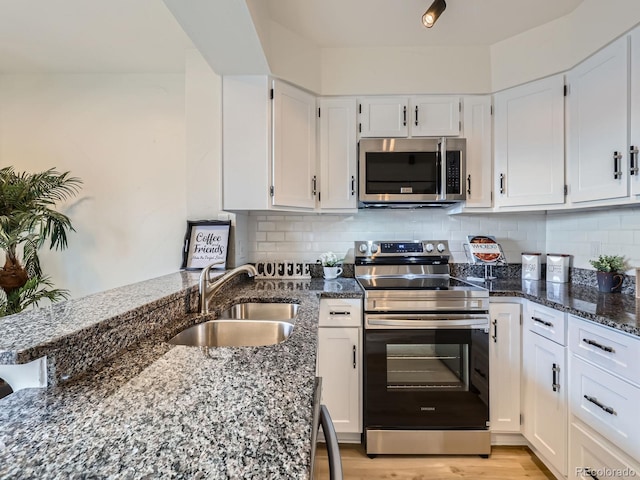 kitchen featuring decorative backsplash, appliances with stainless steel finishes, white cabinets, a sink, and dark stone counters