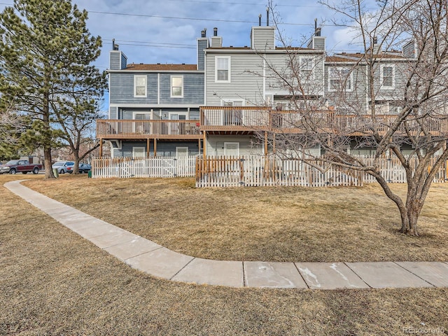 back of house featuring a yard, a chimney, a wooden deck, and fence