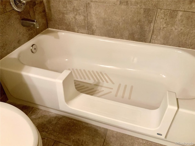 bathroom with a tub to relax in and toilet