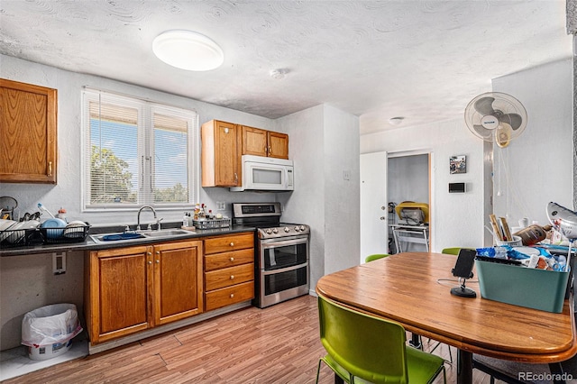 kitchen with a textured ceiling, range with two ovens, light wood-type flooring, and sink