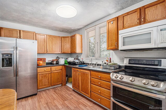 kitchen featuring a textured ceiling, light wood-type flooring, sink, and appliances with stainless steel finishes