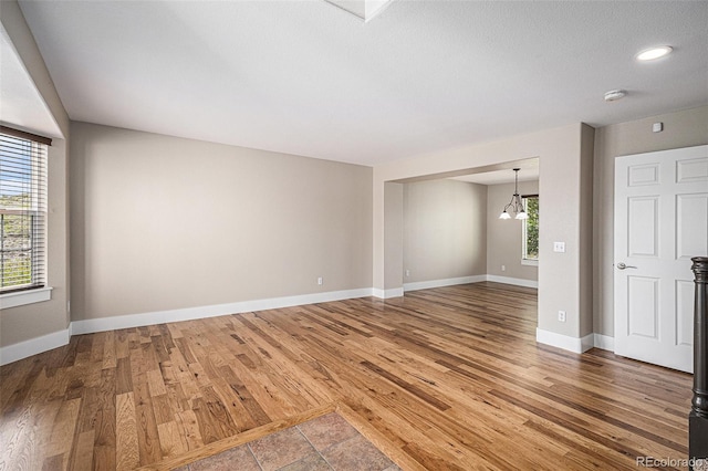 empty room with wood finished floors, baseboards, a chandelier, and recessed lighting