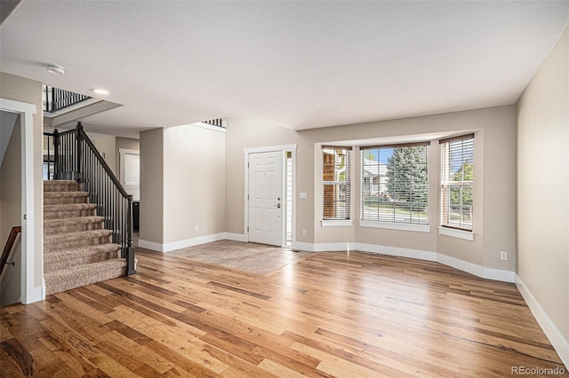 unfurnished living room featuring light wood-style flooring, stairs, and baseboards