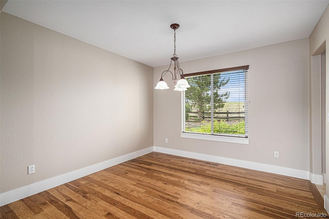 unfurnished room with wood finished floors, baseboards, and a chandelier
