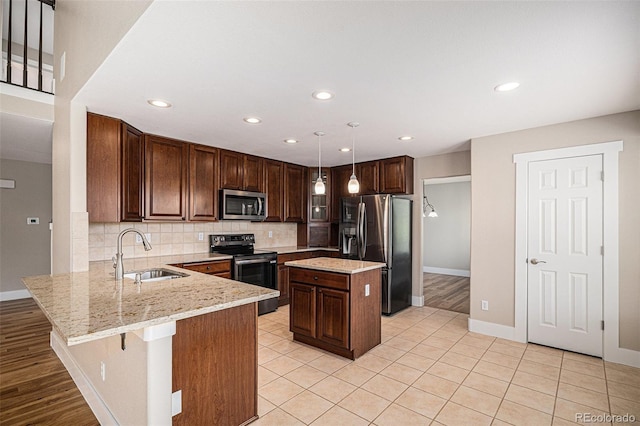 kitchen featuring appliances with stainless steel finishes, a sink, a peninsula, backsplash, and light stone countertops
