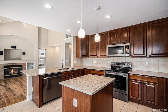 kitchen featuring appliances with stainless steel finishes, a sink, open floor plan, light stone countertops, and light tile patterned floors