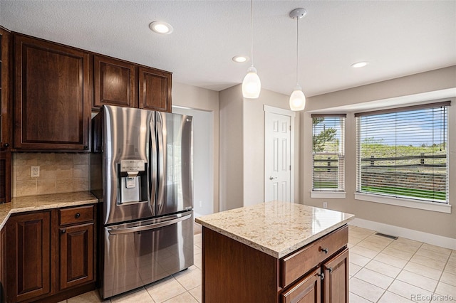 kitchen with stainless steel fridge with ice dispenser, light tile patterned flooring, tasteful backsplash, pendant lighting, and light stone counters