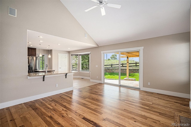 unfurnished living room with light wood-type flooring, baseboards, high vaulted ceiling, ceiling fan, and a sink