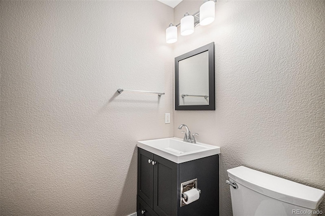 bathroom with toilet, vanity, and a textured wall