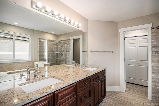 bathroom with a shower stall, double vanity, baseboards, and wood finished floors