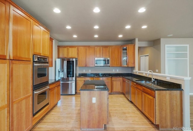 kitchen with a center island, stainless steel appliances, light wood-style floors, a sink, and a peninsula