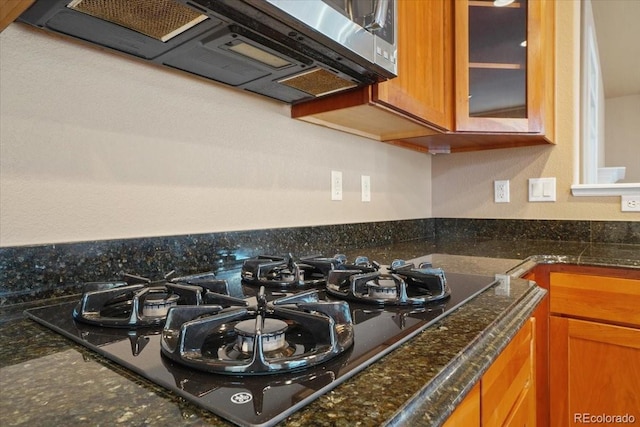 room details with black gas stovetop, stainless steel microwave, glass insert cabinets, and brown cabinetry