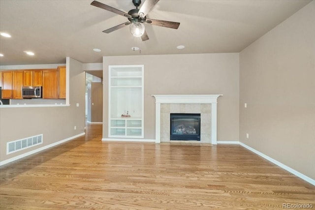 unfurnished living room featuring visible vents, baseboards, a tile fireplace, light wood-style flooring, and ceiling fan