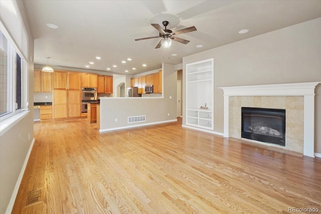 unfurnished living room with light wood finished floors, a tile fireplace, visible vents, and baseboards