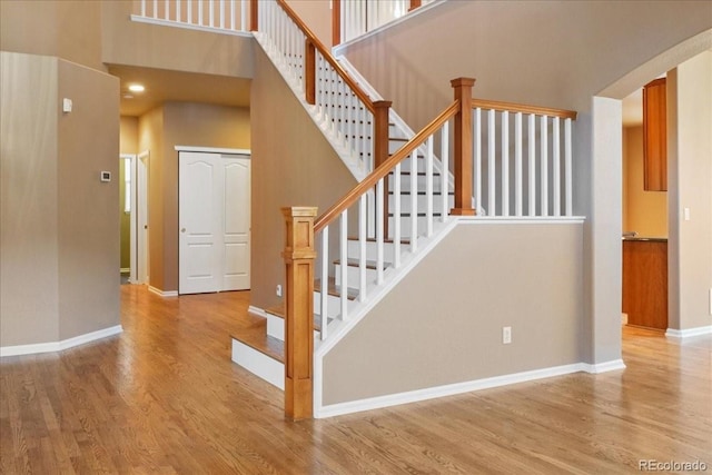 stairs with a high ceiling, wood finished floors, and baseboards