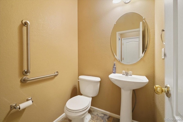 half bath with baseboards, a sink, and toilet