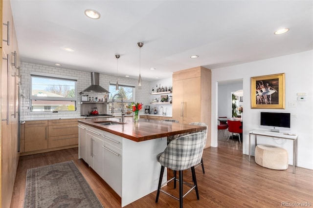 kitchen featuring a breakfast bar, butcher block counters, dark wood-type flooring, a sink, and wall chimney range hood