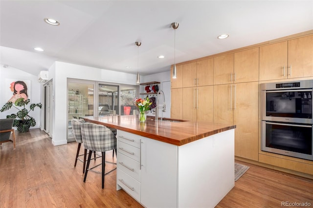 kitchen featuring double oven, a breakfast bar area, a sink, and light wood-style flooring