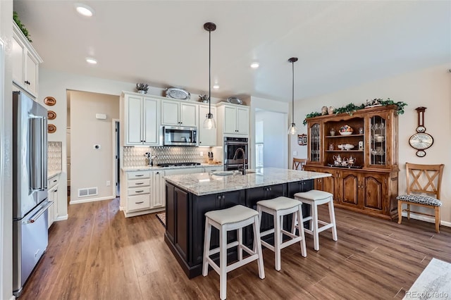 kitchen featuring pendant lighting, white cabinets, stainless steel appliances, and a kitchen island with sink