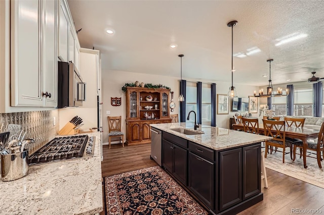 kitchen with light stone countertops, stainless steel appliances, a kitchen island with sink, pendant lighting, and white cabinets