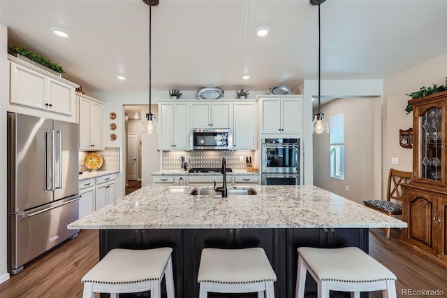 kitchen featuring a center island with sink, hanging light fixtures, backsplash, and appliances with stainless steel finishes