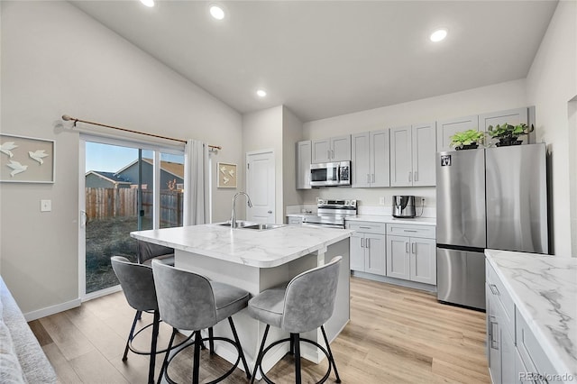 kitchen with an island with sink, appliances with stainless steel finishes, sink, and light stone counters