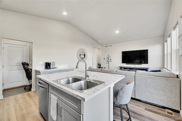 kitchen featuring sink, vaulted ceiling, a center island with sink, light hardwood / wood-style flooring, and stainless steel dishwasher