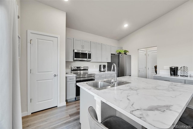 kitchen featuring a kitchen bar, sink, gray cabinets, stainless steel appliances, and a kitchen island with sink