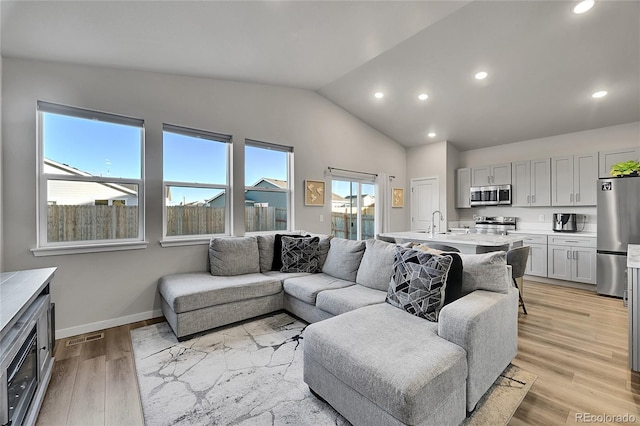 living room featuring vaulted ceiling, sink, and light wood-type flooring