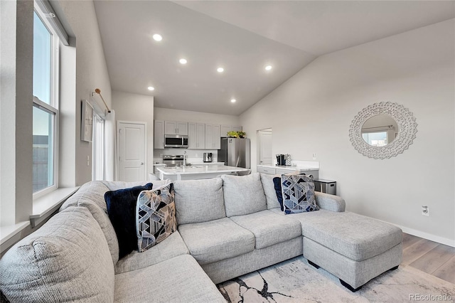 living room featuring high vaulted ceiling, sink, and light hardwood / wood-style floors