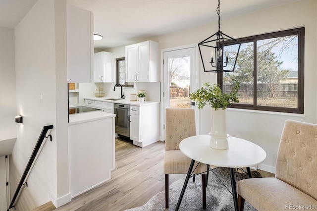 kitchen with stainless steel dishwasher, light wood-type flooring, a sink, light countertops, and a chandelier