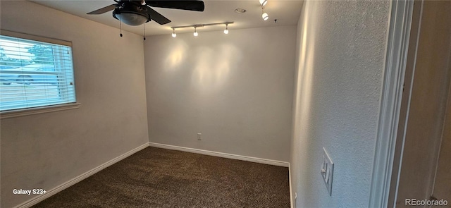 empty room with a ceiling fan, dark colored carpet, track lighting, and baseboards