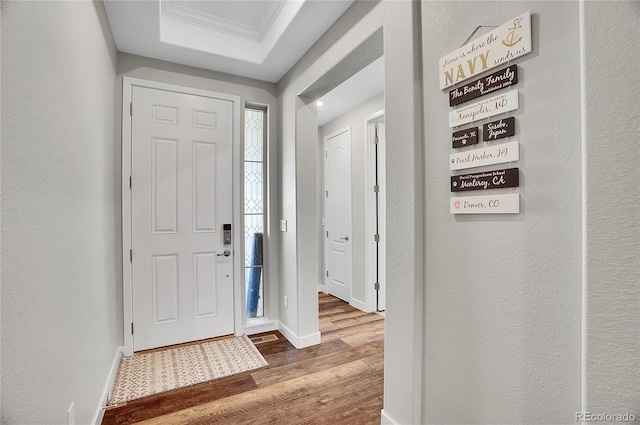 entrance foyer featuring wood finished floors, baseboards, a tray ceiling, crown molding, and a textured wall