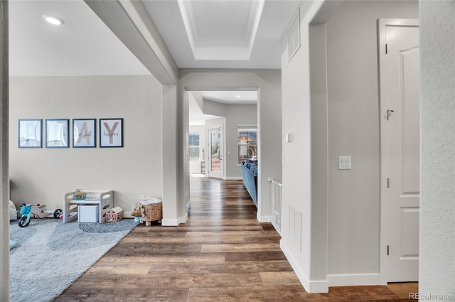 hall with visible vents, baseboards, a tray ceiling, and wood finished floors