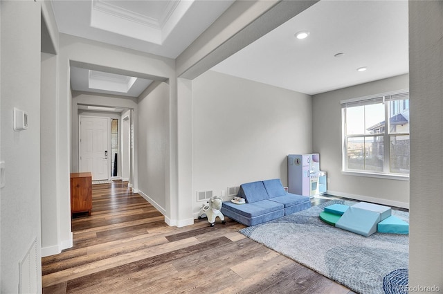 living area with a tray ceiling, baseboards, visible vents, and wood finished floors