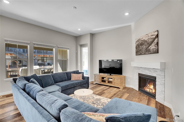 living area featuring recessed lighting, baseboards, a stone fireplace, and wood finished floors