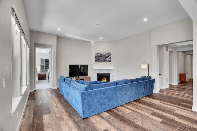 living room with recessed lighting, wood finished floors, and a warm lit fireplace