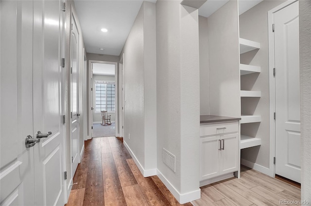 hall with baseboards, visible vents, and light wood finished floors