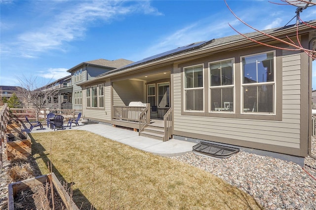 rear view of house with a patio area, roof mounted solar panels, and a lawn