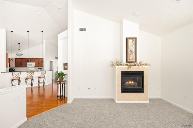 living room featuring lofted ceiling, a tiled fireplace, and light colored carpet