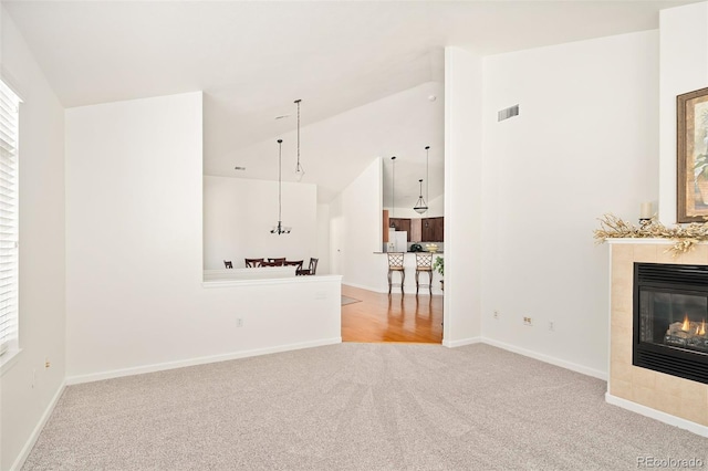 unfurnished living room featuring lofted ceiling, a tiled fireplace, and light carpet