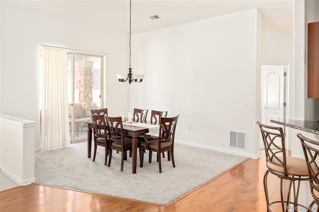 dining space featuring light hardwood / wood-style flooring, an inviting chandelier, and a towering ceiling