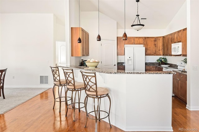 kitchen featuring white appliances, vaulted ceiling, a breakfast bar area, dark stone counters, and pendant lighting