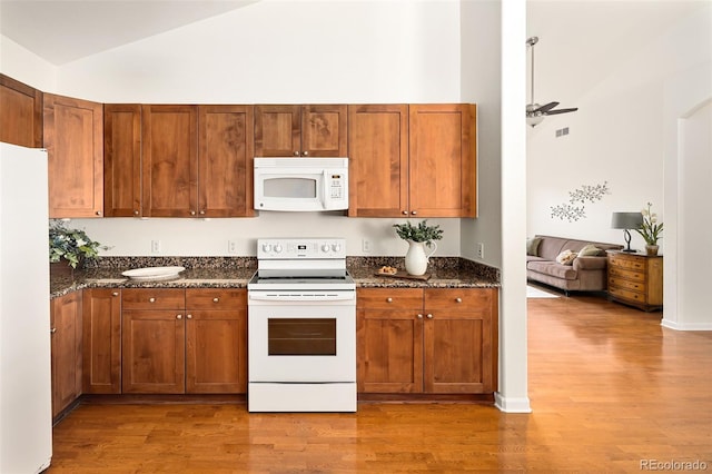 kitchen featuring white appliances, high vaulted ceiling, dark stone counters, and hardwood / wood-style floors