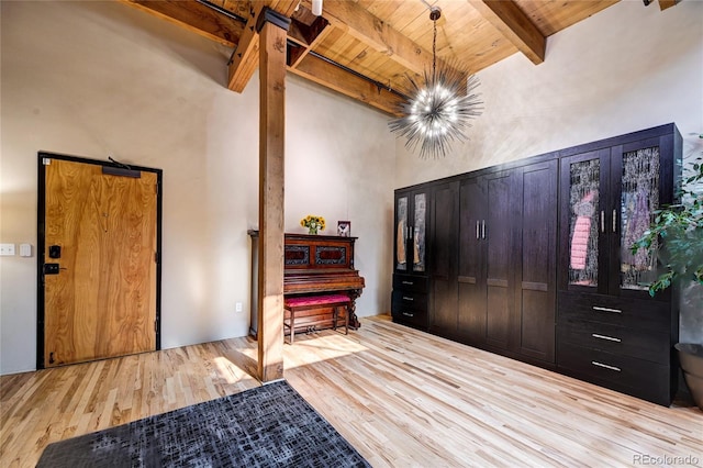 foyer entrance featuring a towering ceiling, beam ceiling, wooden ceiling, a notable chandelier, and light hardwood / wood-style floors