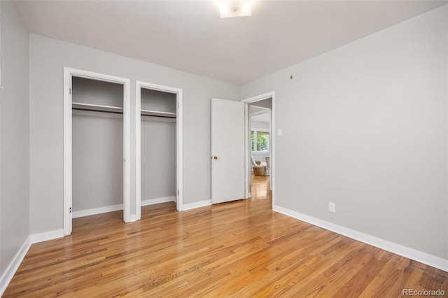 unfurnished bedroom with light wood-style floors, two closets, and baseboards