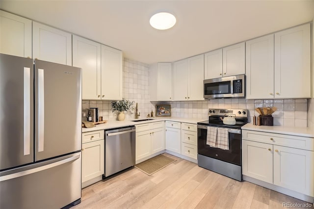 kitchen featuring appliances with stainless steel finishes, light hardwood / wood-style floors, sink, white cabinets, and tasteful backsplash