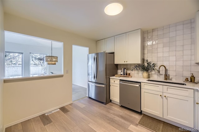 kitchen featuring hanging light fixtures, stainless steel appliances, backsplash, white cabinets, and sink