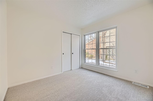 spare room featuring light colored carpet and a textured ceiling